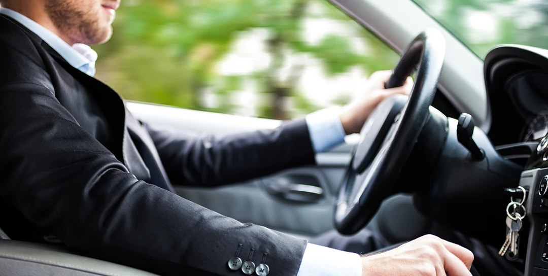 Man behind steering wheel of a car; driving.