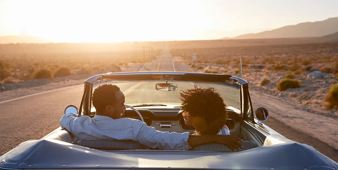 Two people in a car heading down highway into horizon.
