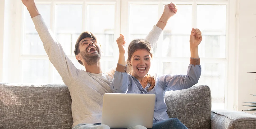 Man and woman celebrating on a couch looking at a laptop.
