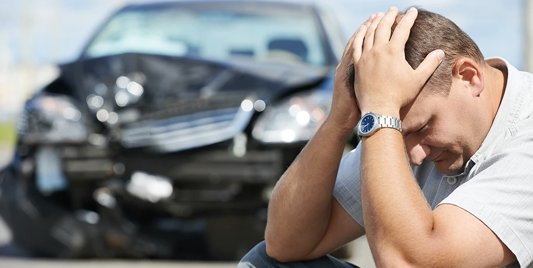 Man with head in hands in front of wrecked car.