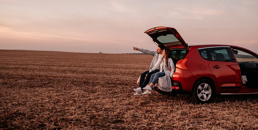 Man and woman sitting on back bumper pointing at sky.