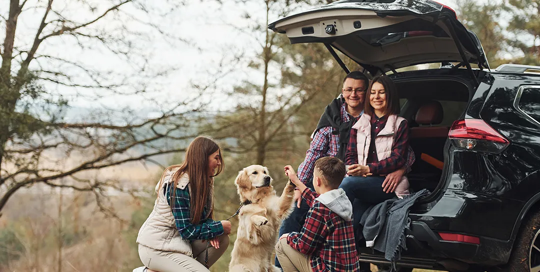 Family with back of car open playing with dog.