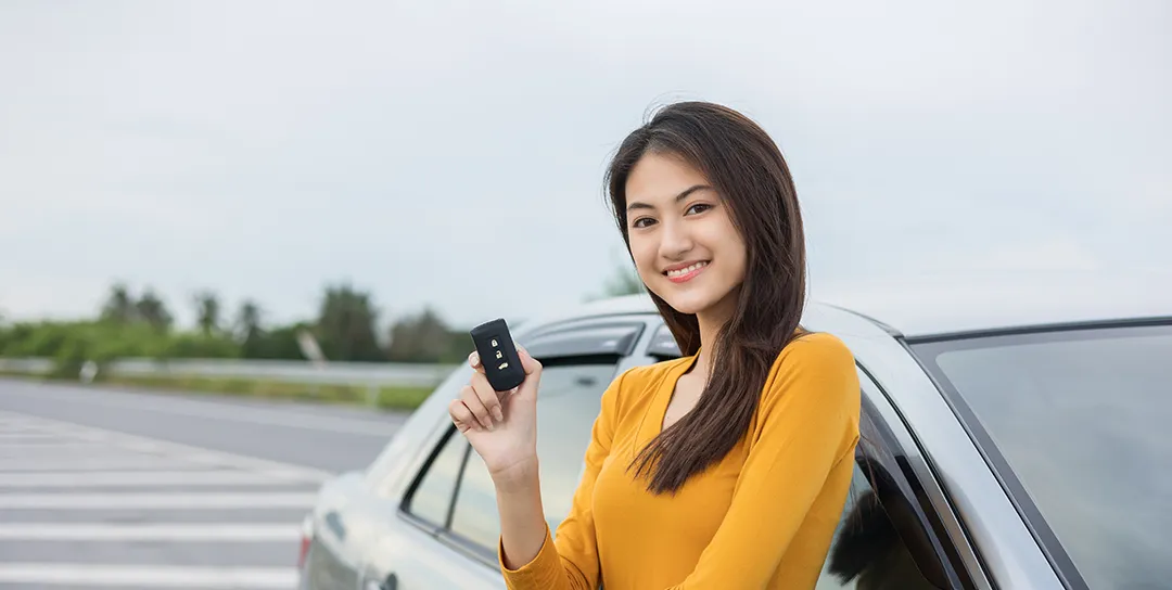 Girl standing against passenger side of car holding key.