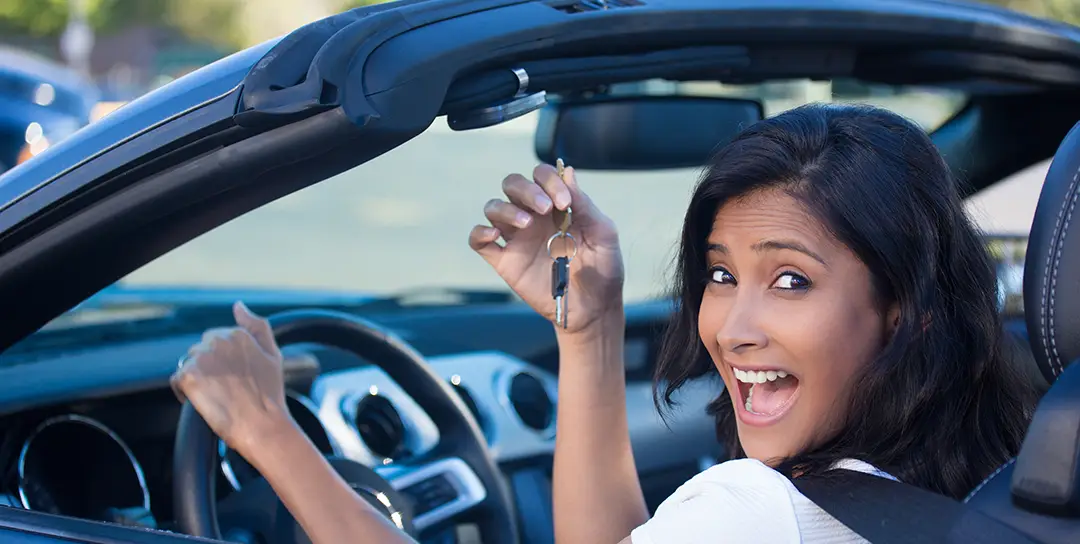 Girl in convertible car with key held up in front of her smiling.
