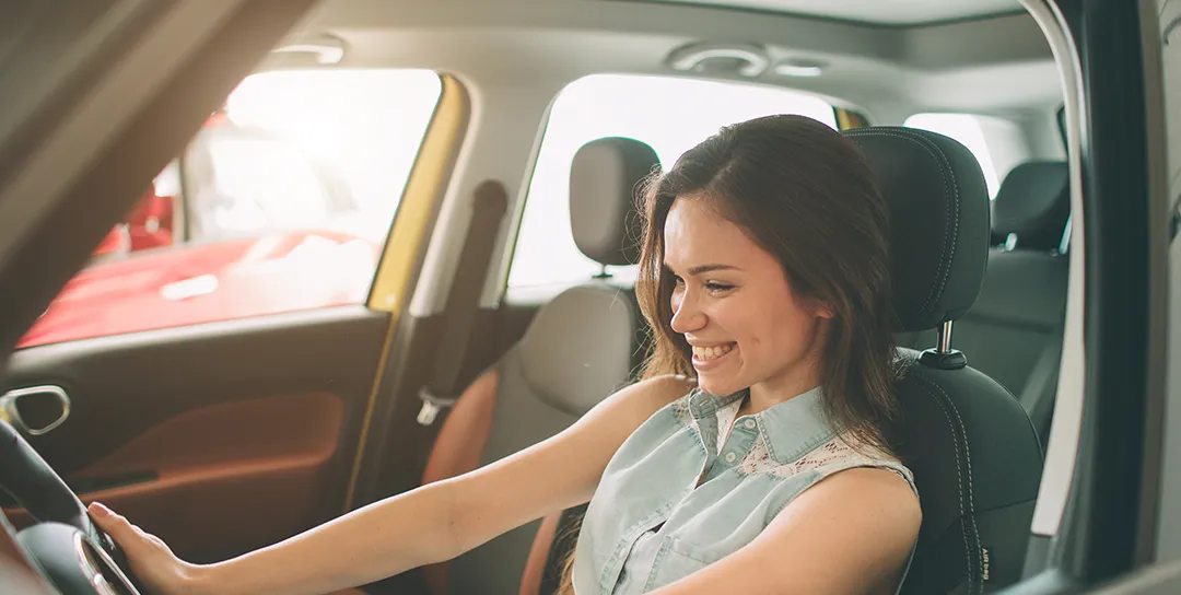 Girl smiling and sitting in driver's seat.