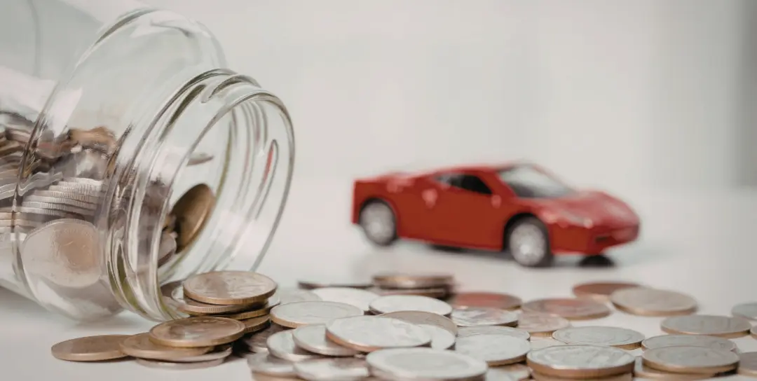A jar of coins spilling out on its side sits in front of a blurred red toy car.