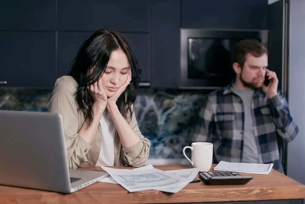 Couple dealing with financial stress at home, surrounded by bills and a laptop.