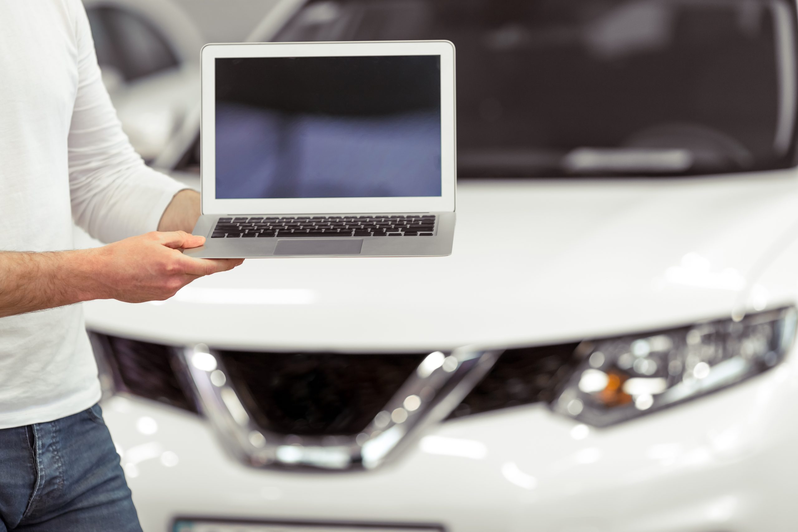 Person holding a computer in front of a white car.