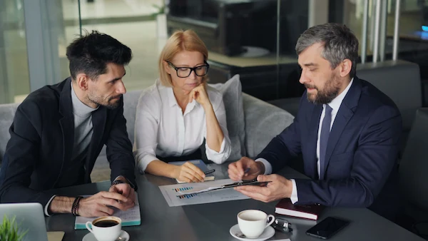 Three professionals engaged in a business discussion at an office table with coffee.